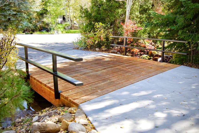 Wooden bridge with metal railings crossing a stream, surrounded by autumn foliage.