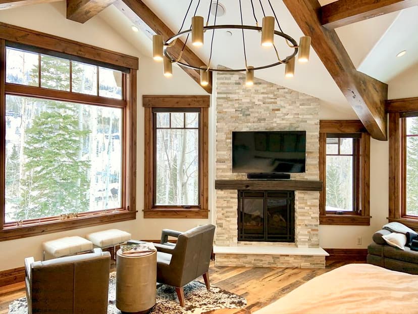 Modern living room with large windows, stylish furniture, and a stone fireplace in a snowy retreat.