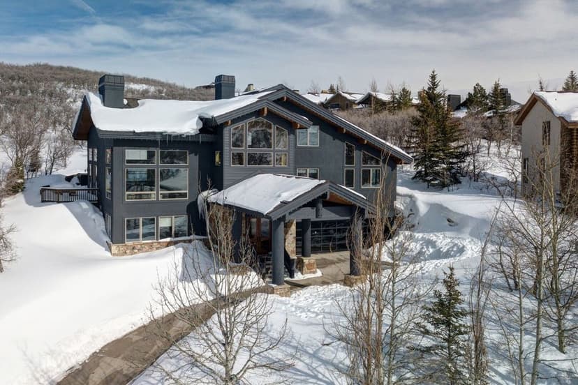 Modern mountain home surrounded by snow, featuring large windows and a stone driveway.